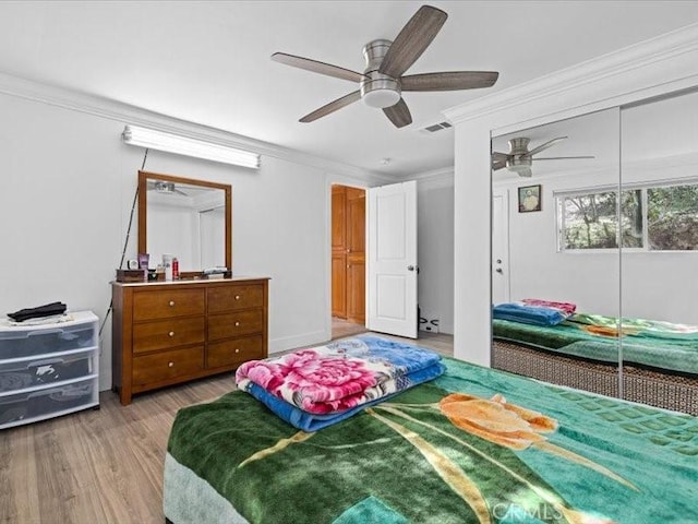 bedroom with wood finished floors, visible vents, a ceiling fan, ornamental molding, and a closet