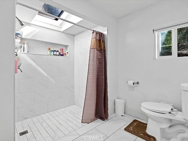 bathroom featuring a skylight, baseboards, toilet, marble finish floor, and a tile shower