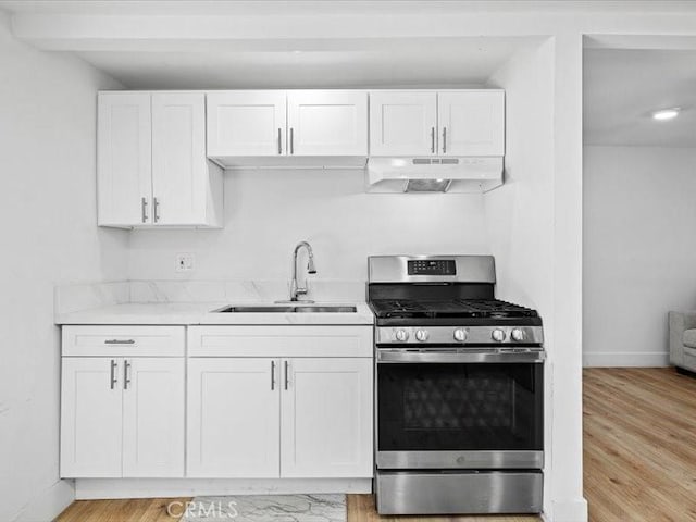 kitchen featuring under cabinet range hood, a sink, white cabinetry, light wood finished floors, and gas range