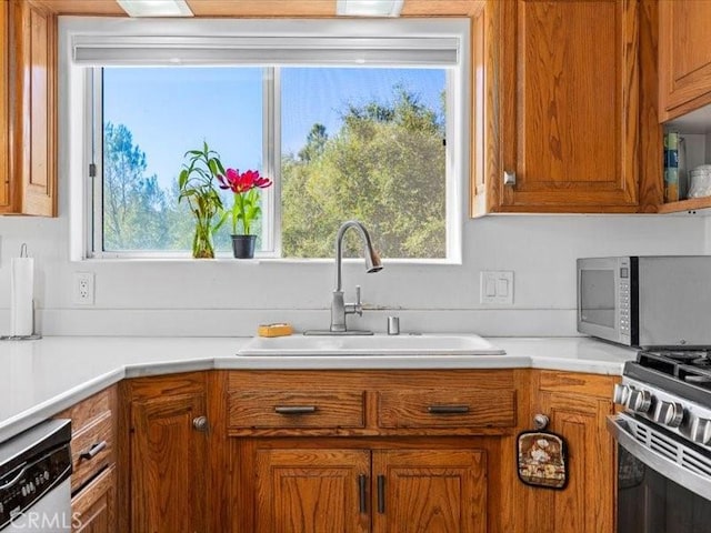 kitchen featuring brown cabinets, stainless steel appliances, a sink, and light countertops