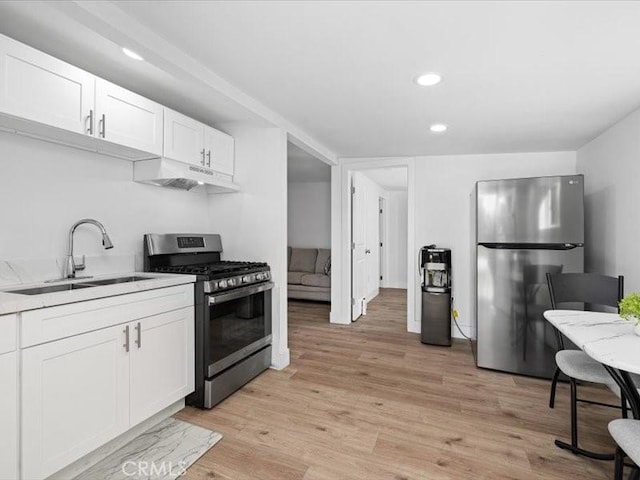 kitchen featuring under cabinet range hood, a sink, white cabinetry, light wood-style floors, and appliances with stainless steel finishes