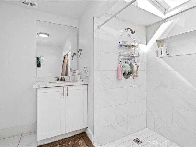 bathroom featuring visible vents, vanity, baseboards, and tiled shower