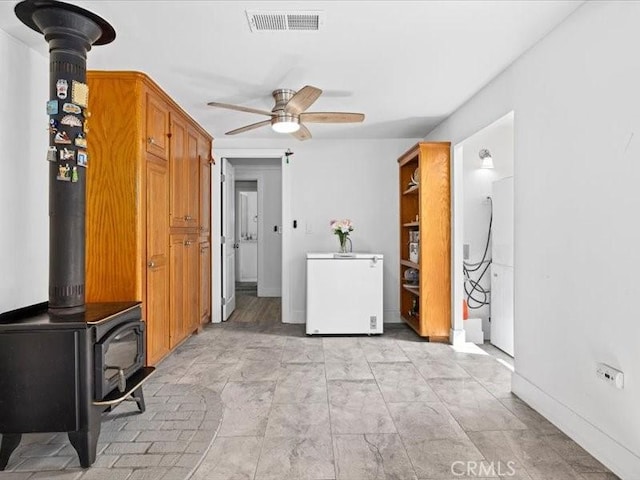 washroom with a wood stove, ceiling fan, visible vents, and baseboards