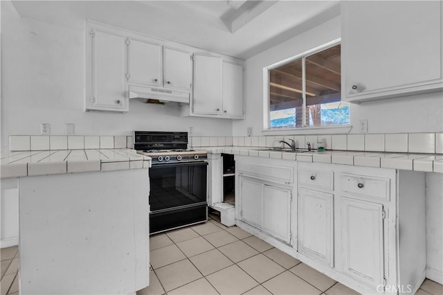 kitchen featuring range with gas cooktop, tile countertops, white cabinetry, a sink, and under cabinet range hood