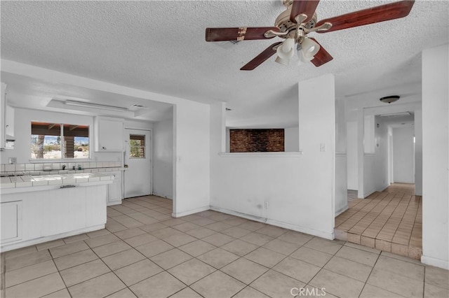 kitchen with light tile patterned floors, tile counters, white cabinets, a ceiling fan, and a textured ceiling