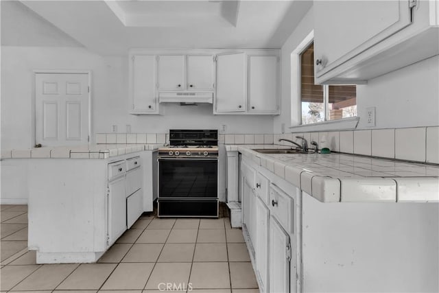 kitchen featuring range with gas stovetop, white cabinets, a sink, a peninsula, and under cabinet range hood