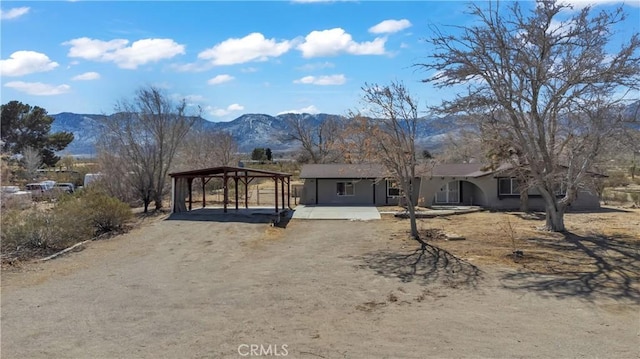 single story home with dirt driveway, a mountain view, and a detached carport