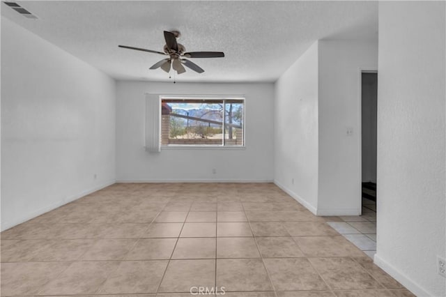 tiled empty room with baseboards, ceiling fan, visible vents, and a textured ceiling