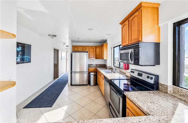 kitchen with light tile patterned floors, plenty of natural light, light stone counters, stainless steel appliances, and a sink