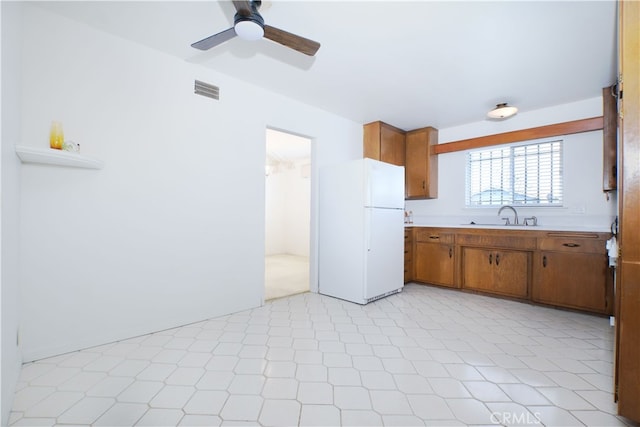 kitchen featuring brown cabinets, light countertops, visible vents, freestanding refrigerator, and a sink