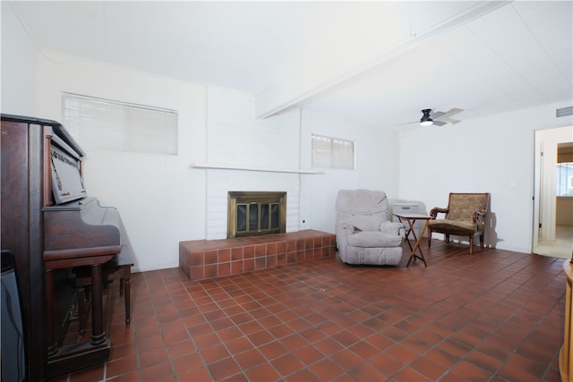 sitting room featuring a brick fireplace, visible vents, beamed ceiling, and ceiling fan