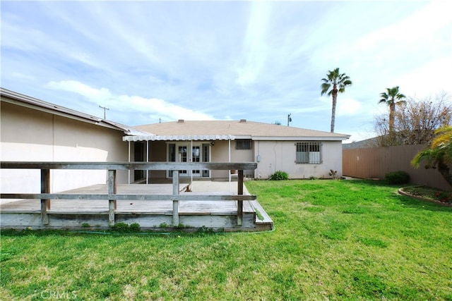 back of house featuring stucco siding, a wooden deck, fence, and a yard