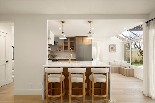 kitchen featuring a breakfast bar area, a peninsula, light wood-style floors, stainless steel fridge, and glass insert cabinets