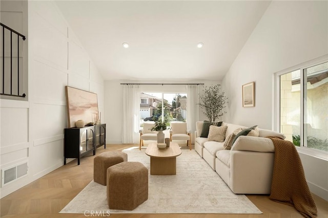 living area with high vaulted ceiling, visible vents, a decorative wall, and recessed lighting