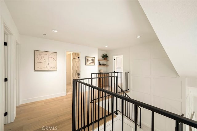 hall featuring light wood finished floors, recessed lighting, baseboards, and an upstairs landing