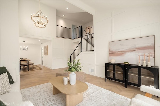 living area with recessed lighting, a decorative wall, a towering ceiling, stairway, and an inviting chandelier