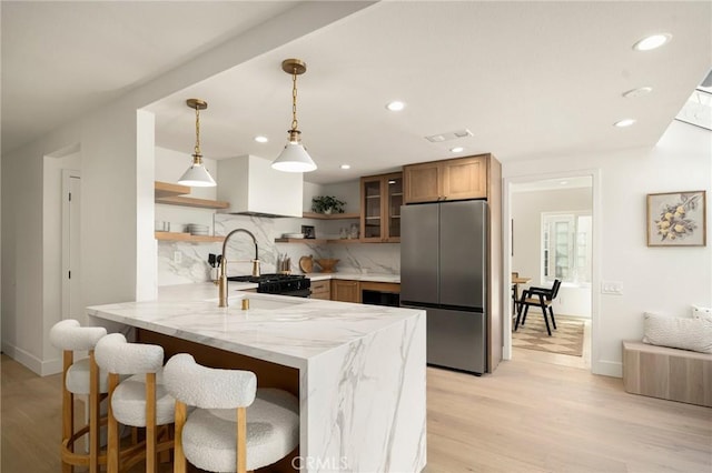 kitchen with light stone counters, a peninsula, a sink, open shelves, and stainless steel fridge