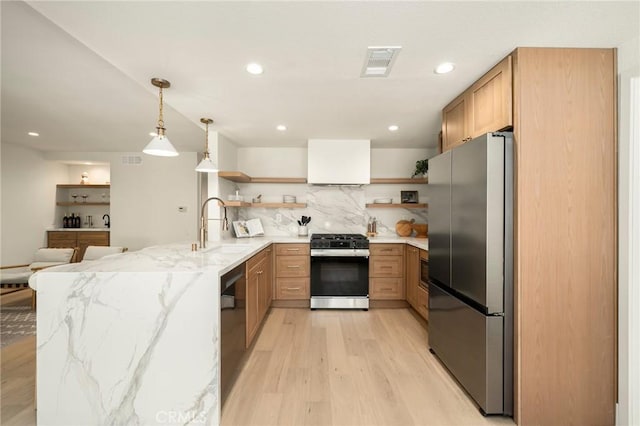 kitchen featuring range with gas stovetop, open shelves, freestanding refrigerator, a sink, and a peninsula