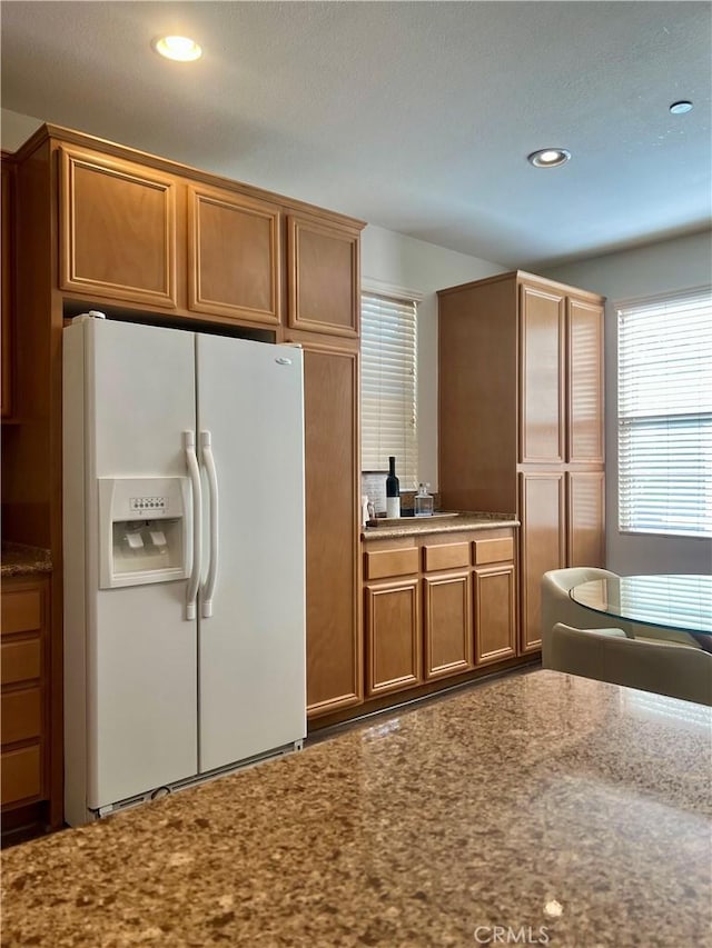 kitchen featuring stone counters, white fridge with ice dispenser, brown cabinets, and recessed lighting