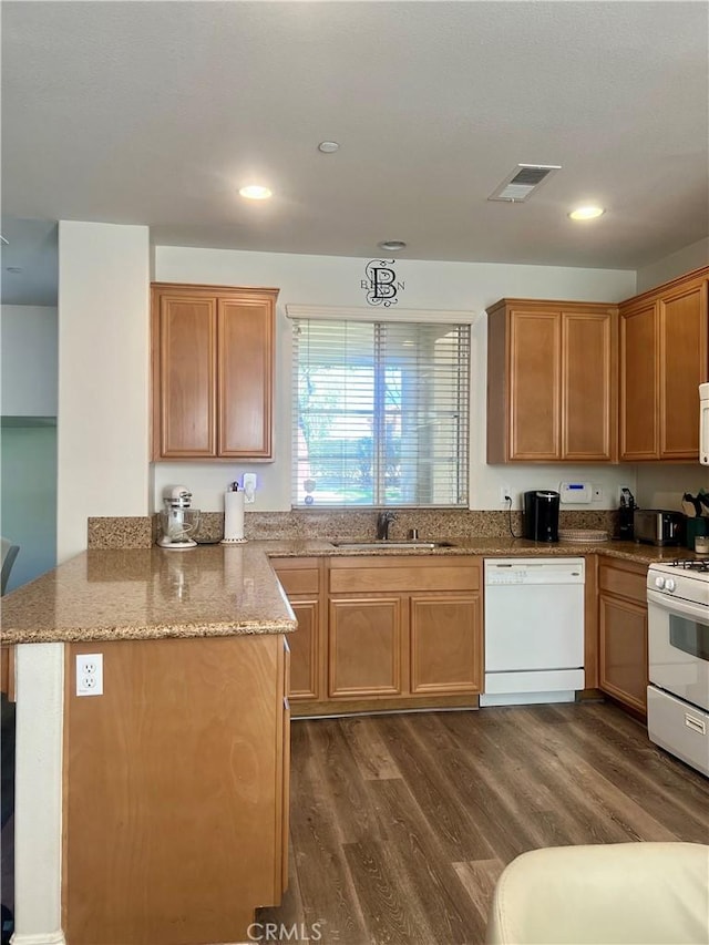 kitchen featuring light stone counters, visible vents, a sink, white appliances, and a peninsula