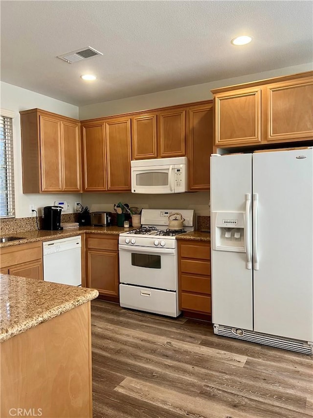 kitchen with white appliances, visible vents, dark wood finished floors, light stone countertops, and a sink