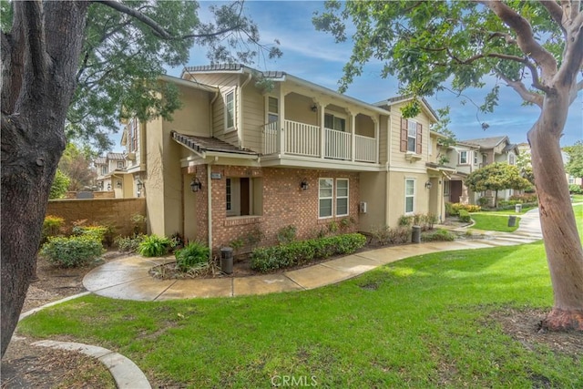 back of property featuring a balcony, a yard, brick siding, and stucco siding