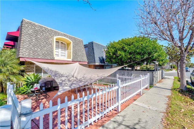 view of home's exterior featuring mansard roof, roof with shingles, and a fenced front yard