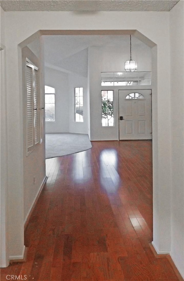 foyer entrance with baseboards, wood-type flooring, a textured ceiling, and a chandelier