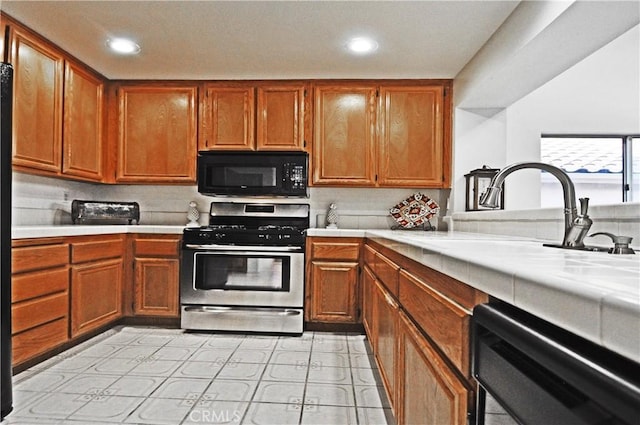 kitchen featuring stainless steel gas range oven, dishwashing machine, brown cabinetry, and black microwave