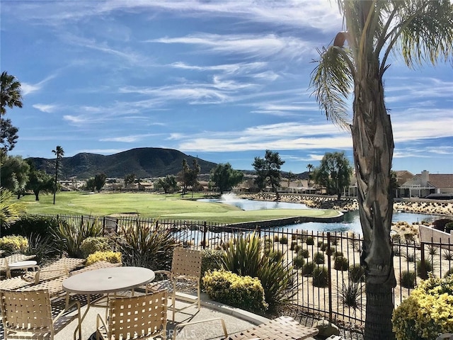 view of patio with outdoor dining space, view of golf course, a water and mountain view, and fence