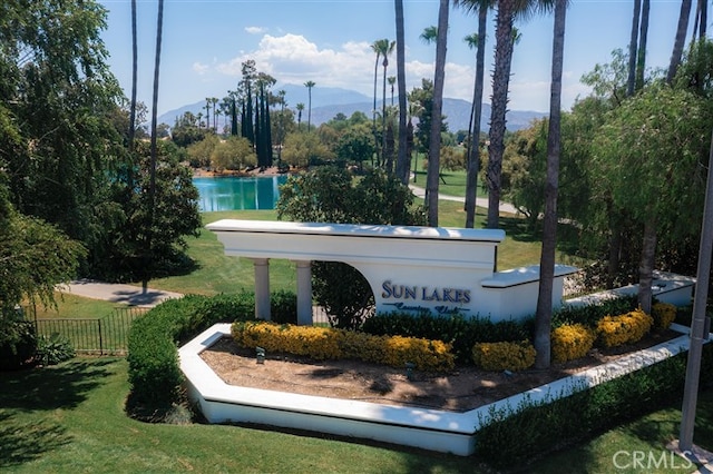 community / neighborhood sign with fence, a lawn, and a water and mountain view