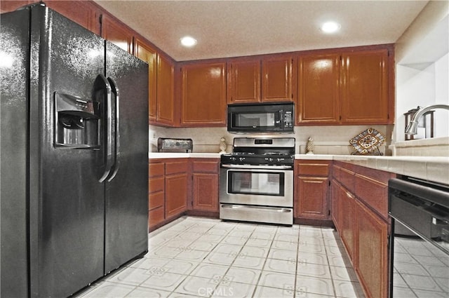 kitchen featuring recessed lighting, brown cabinets, black appliances, and tile counters