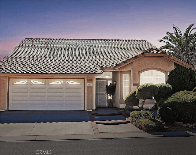 view of front of house featuring stucco siding, a garage, concrete driveway, and a tile roof