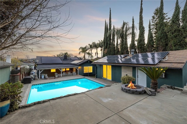 pool at dusk with an outdoor fire pit, a patio area, fence, and an outdoor pool