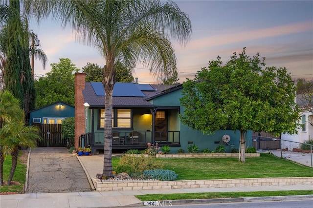 view of front of property with a lawn, covered porch, fence, roof mounted solar panels, and stucco siding