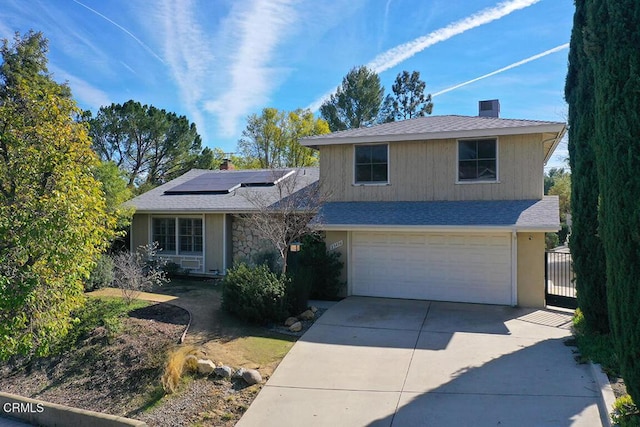 view of front facade with roof with shingles, a chimney, concrete driveway, roof mounted solar panels, and a garage