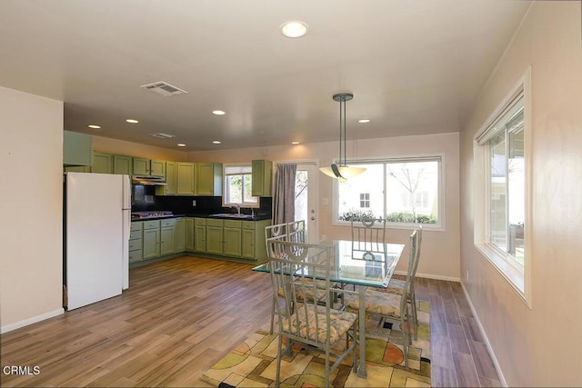 kitchen with under cabinet range hood, a sink, visible vents, freestanding refrigerator, and green cabinetry