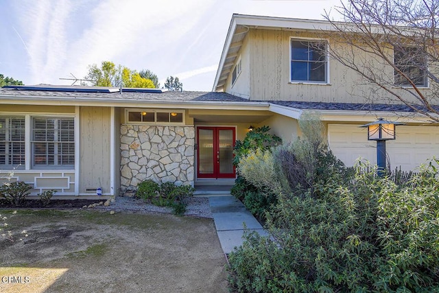 view of front of property featuring an attached garage, stone siding, solar panels, and french doors