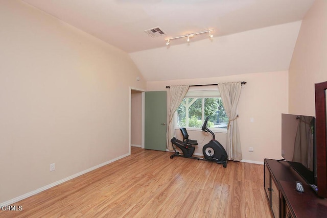 exercise area featuring light wood finished floors, rail lighting, visible vents, vaulted ceiling, and baseboards