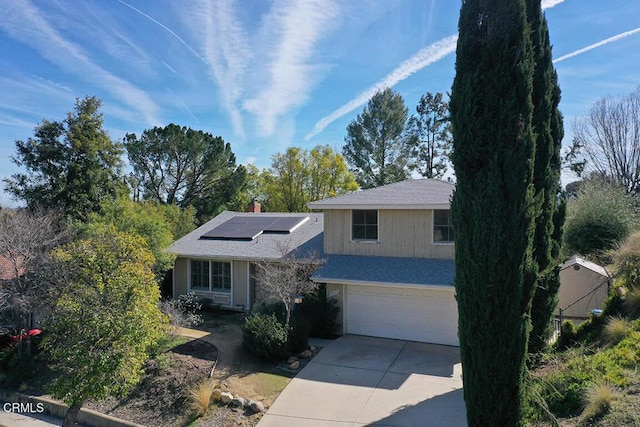 view of front of house with driveway, a chimney, an attached garage, and roof mounted solar panels