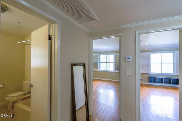 corridor with ornamental molding, visible vents, baseboards, and wood finished floors