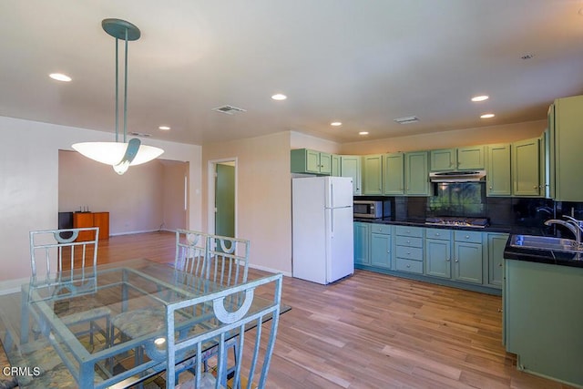 kitchen with stainless steel appliances, light wood-type flooring, under cabinet range hood, green cabinets, and a sink