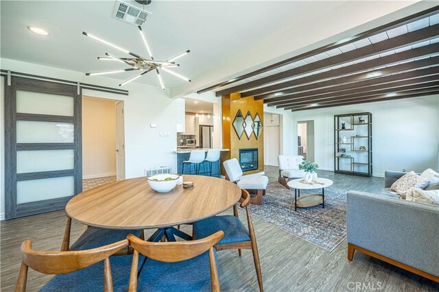 dining space with a barn door, visible vents, wood finished floors, and a glass covered fireplace