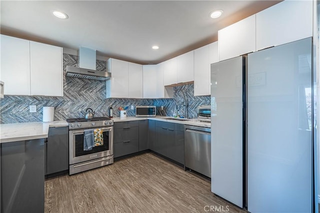 kitchen with stainless steel appliances, wood finished floors, gray cabinets, wall chimney exhaust hood, and modern cabinets