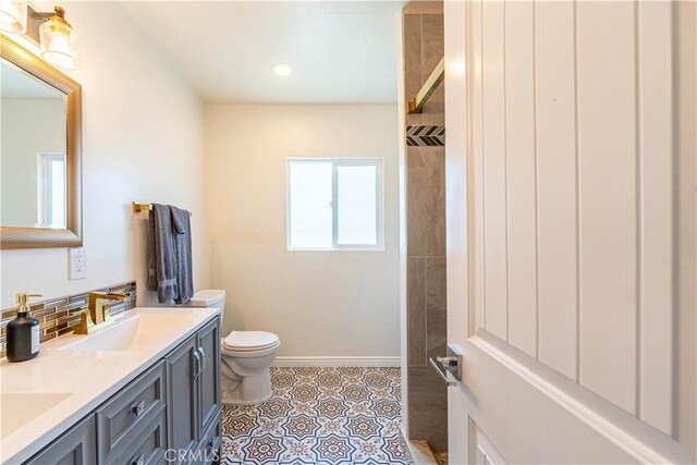 bathroom featuring double vanity, backsplash, toilet, a sink, and baseboards