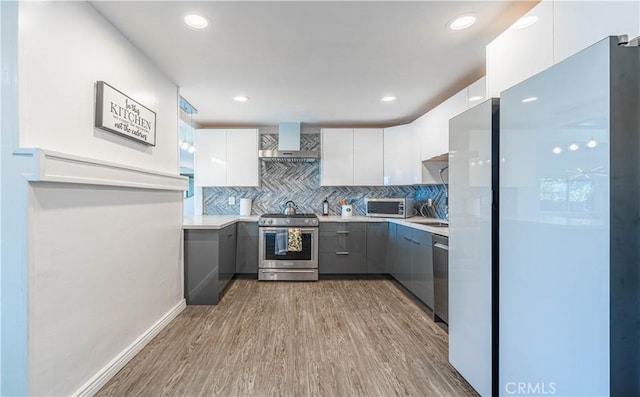 kitchen featuring wall chimney exhaust hood, modern cabinets, appliances with stainless steel finishes, gray cabinets, and light wood-type flooring