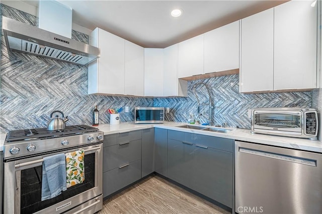 kitchen featuring wall chimney exhaust hood, appliances with stainless steel finishes, light countertops, and backsplash