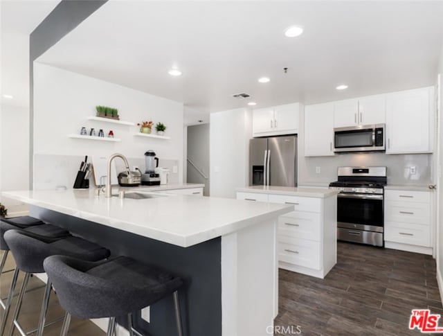 kitchen featuring dark wood-type flooring, a peninsula, stainless steel appliances, open shelves, and a sink