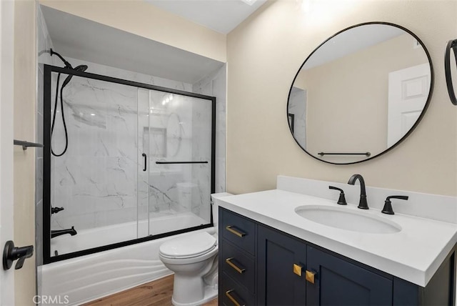 bathroom featuring enclosed tub / shower combo, vanity, toilet, and wood finished floors