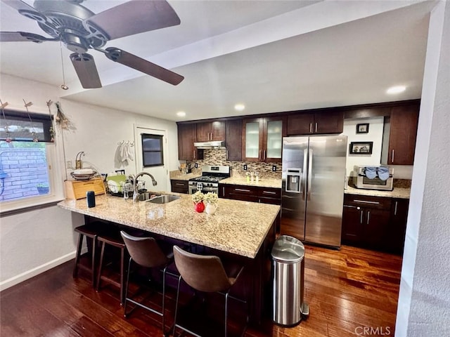 kitchen with under cabinet range hood, stainless steel appliances, a breakfast bar, a sink, and dark wood-style floors